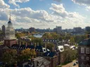 Skyline view of Harvard University with trees in autumn colors and a river under a cloudy sky.