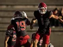 Two Harvard football players celebrate a play, with one jumping excitedly in a stadium.