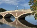 Weeks footbridge with its arches reflected in calm water under a blue sky.