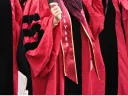 Close-up of a graduate's arm in a red robe with "Harvard" sash during a ceremony.