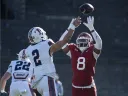 Harvard football player in red attempts to block a pass from a Penn player in white during a game.