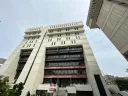 Tall modern building with multiple floors and large windows against a cloudy sky.
