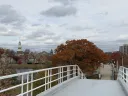 View from a bridge with autumn trees and a cloudy sky in the background.