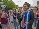 A jubilant graduate shouts into a megaphone, surrounded by a cheering crowd.