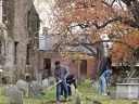 A student uses a shovel to clear debris and weeds from graves in a cemetery