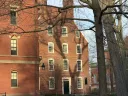 Historic red brick building with large windows and tree shadows in foreground.