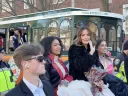 A group of elegantly dressed individuals poses near a parade trolley, smiling and celebrating.
