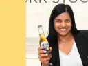A woman in a black blazer holds a bottle of beer.