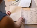 A person examining handwritten notes and papers on a table.