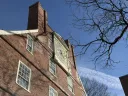 Brick building with a large clock and tree branches against a clear blue sky.