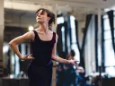 A dancer in a black leotard poses gracefully in a bright studio, with mirrors reflecting her movement.