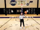 Katie Benzan stands on a basketball court holding a ball, with a hoop in the background.
