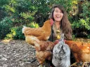 Alene Anello smiling surrounded by four chickens in a natural outdoor setting.