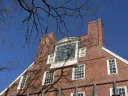 Massachusetts Hall under a clear blue sky, showcasing a prominent clock and large windows.