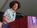 A man smiles while speaking at a podium with a Harvard logo.