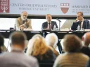 Three speakers at a panel discussion in front of an audience, with Harvard branding.