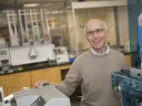 Smiling man with glasses in a laboratory, standing beside equipment.