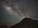 Star-filled night sky with the Milky Way arching over a rocky silhouette.