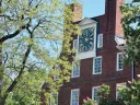 Massachusetts Hall at Harvard Red brick building with a large clock on top, surrounded by green trees.