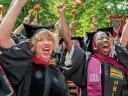 Graduates in caps and gowns celebrate joyfully, raising their hands in excitement.