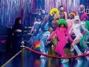 A vibrant group of dancers in colorful outfits poses on a stage with shiny decorations.