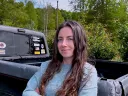 A woman with long hair stands confidently with crossed arms next to a pickup truck.