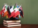 Assorted national flags arranged on a stack of books against a green background.