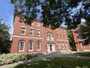 Red brick building with large windows and greenery, set against a bright blue sky.