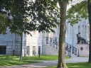 University Hall with steps and the John Harvard statue, surrounded by trees and a grassy lawn.