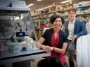 Two laboratory researchers, one seated and one standing, in a scientific lab with equipment.