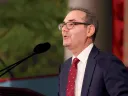 A man in a suit speaks at a podium.