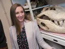 Smiling woman stands beside a large skull in a display cabinet.
