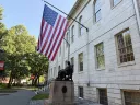 John Harvard statue under the American Flag 