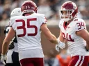 Two Harvard football players in white uniforms slap hands.