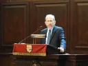 Man wearing a suit stands at a podium and speaks into a microphone.