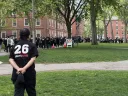 A crowd of people in black shirts gathers in a park with green grass and trees.