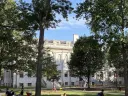 Historic building surrounded by trees, with people gathering in a park setting.