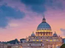 St. Peter's Basilica at sunset, illuminated by purple and orange sky reflections in the river.
