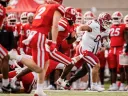 A football player in white uniform evades tackle from red jersey opponents on the field.