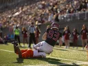 A football player in black and red gear catches the ball near the orange end zone marker.