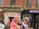 Elizabeth Banks looks at the camera as she rides in a convertible with two members of the Hasty Pudding Theatricals.
