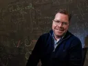 Louis Deslauriers seated at a table in front of a blackboard