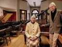 An older couple standing in a large room filled with pianos