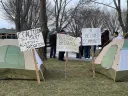 Tents and signs foreground a photograph of a rally in Allston organized by the Coalition for a Just Allston-Brighton on Tuesday, March 15