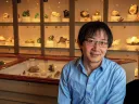 Roger Fu sits in front of a display case of rock samples