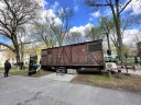 A red-brown train car with boarded-up windows, harsh metal siding, and faded industrial German lettering is on display in Harvard Yard.