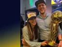 Balcetis smiling and holding the NBA championship trophy, with his arm around his wife