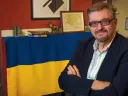 Serhii Plokhy in his Harvard office, smiling with his arms crossed. Behind him hangs a Ukrainian flag signed by Kyiv mayor Vitali Klitschko