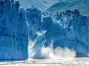 A photograph of a glacier breaking apart in Alaska, with large chunks of ice falling into the ocean.