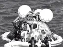 A man in a wetsuit helps an astronaut out of an Apollo capsule floating in the ocean